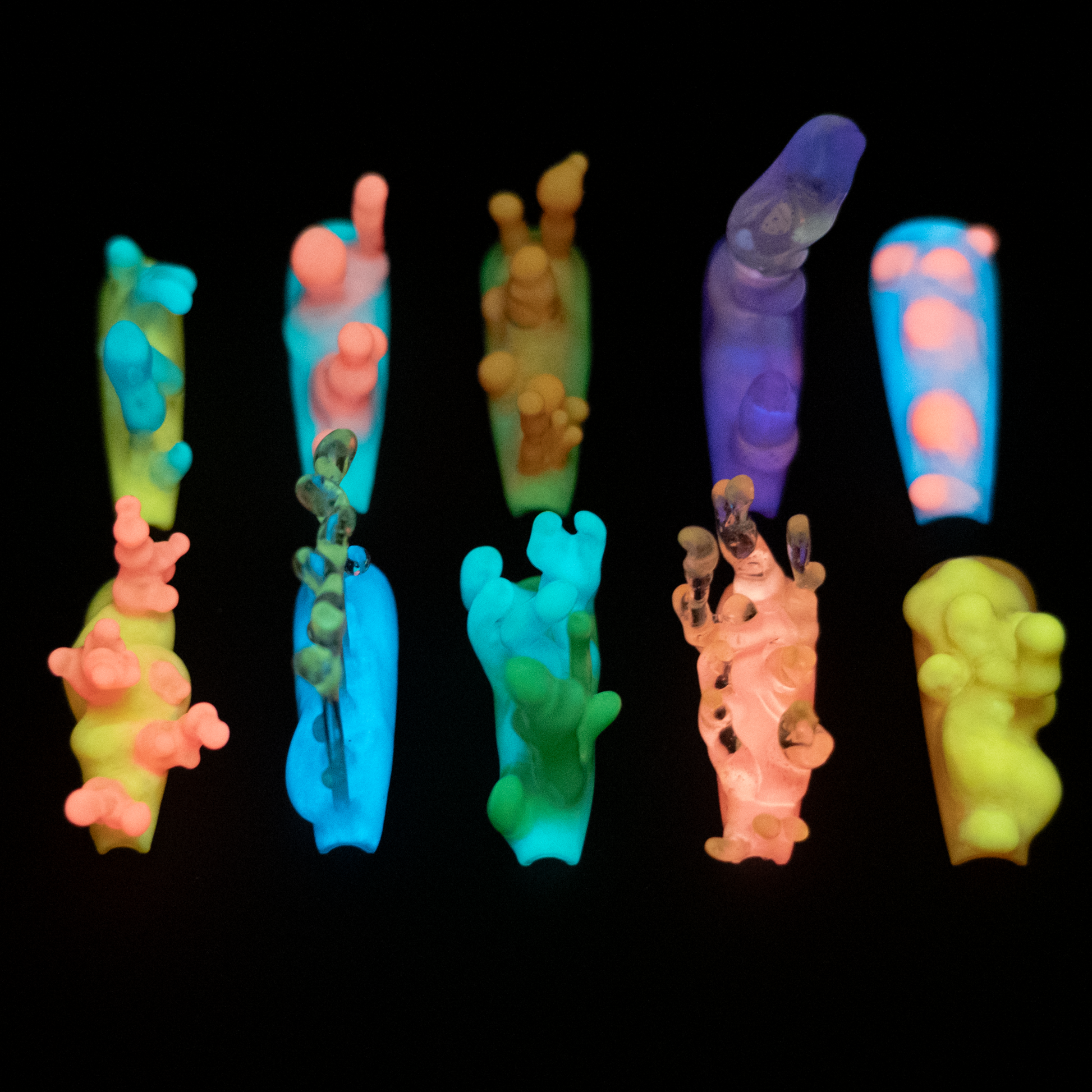 A collection of vibrant, neon handmade press-on nails glowing in dark, resembling colorful nudibranchs or lava lamps with unique textures.