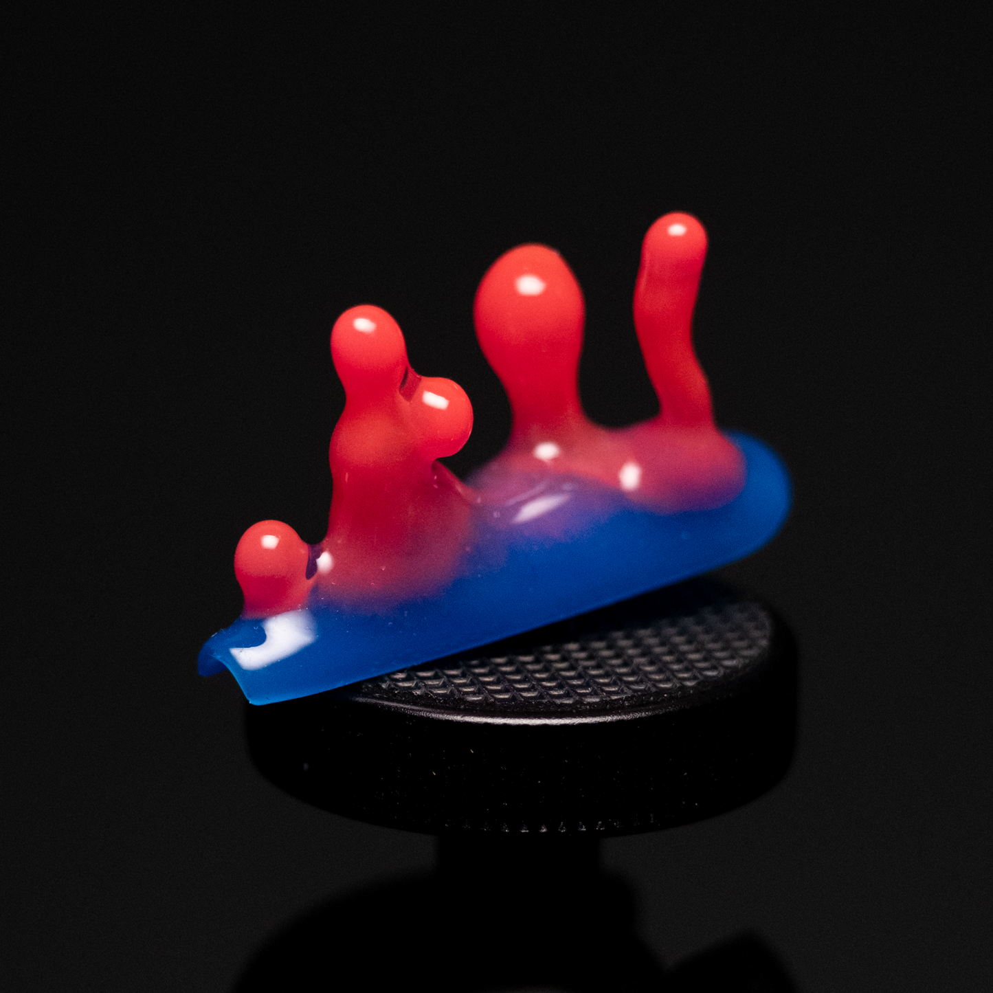 A close-up of a handmade press-on nail with a vibrant blue base transitioning into bright red, featuring bulbous shapes emerging from the surface, resembling playful droplets.