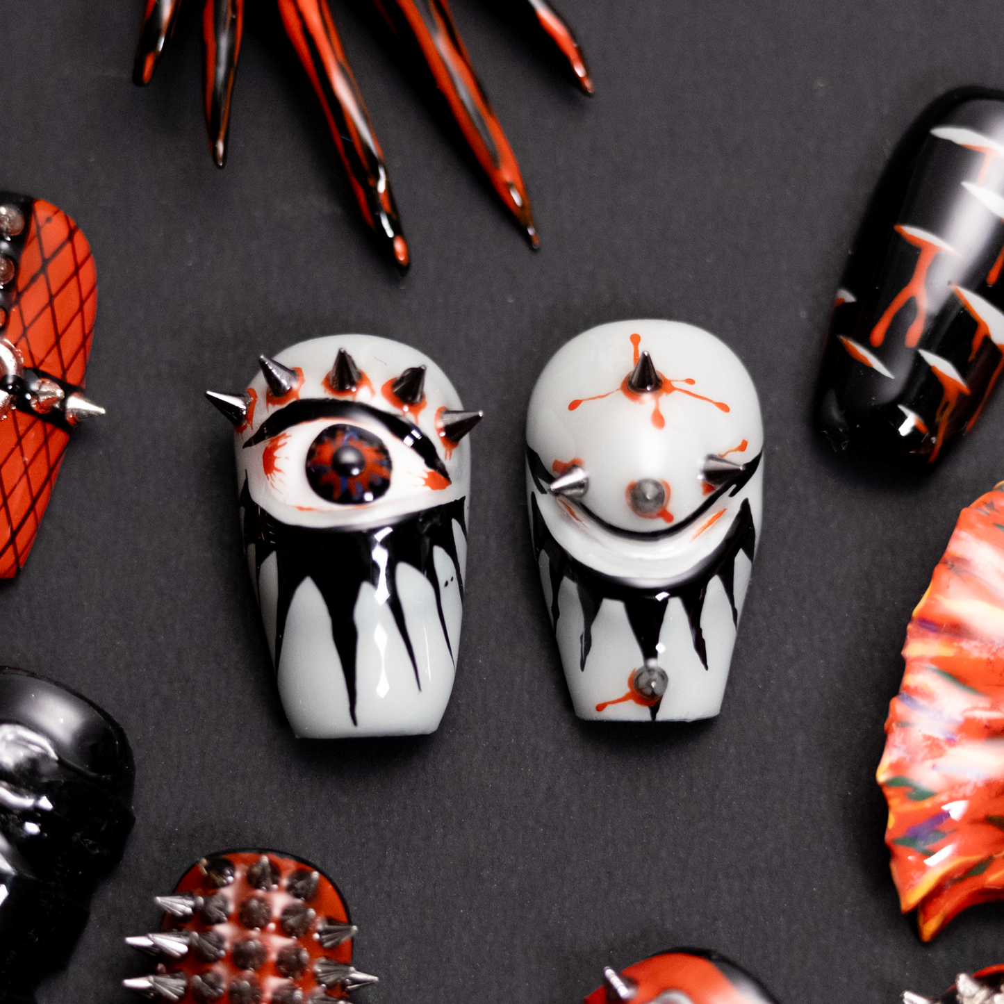 A close-up of two bold press-on nails featuring an eye and smiley face with spikes, black and red dripping effects, embodying a rebellious punk style.