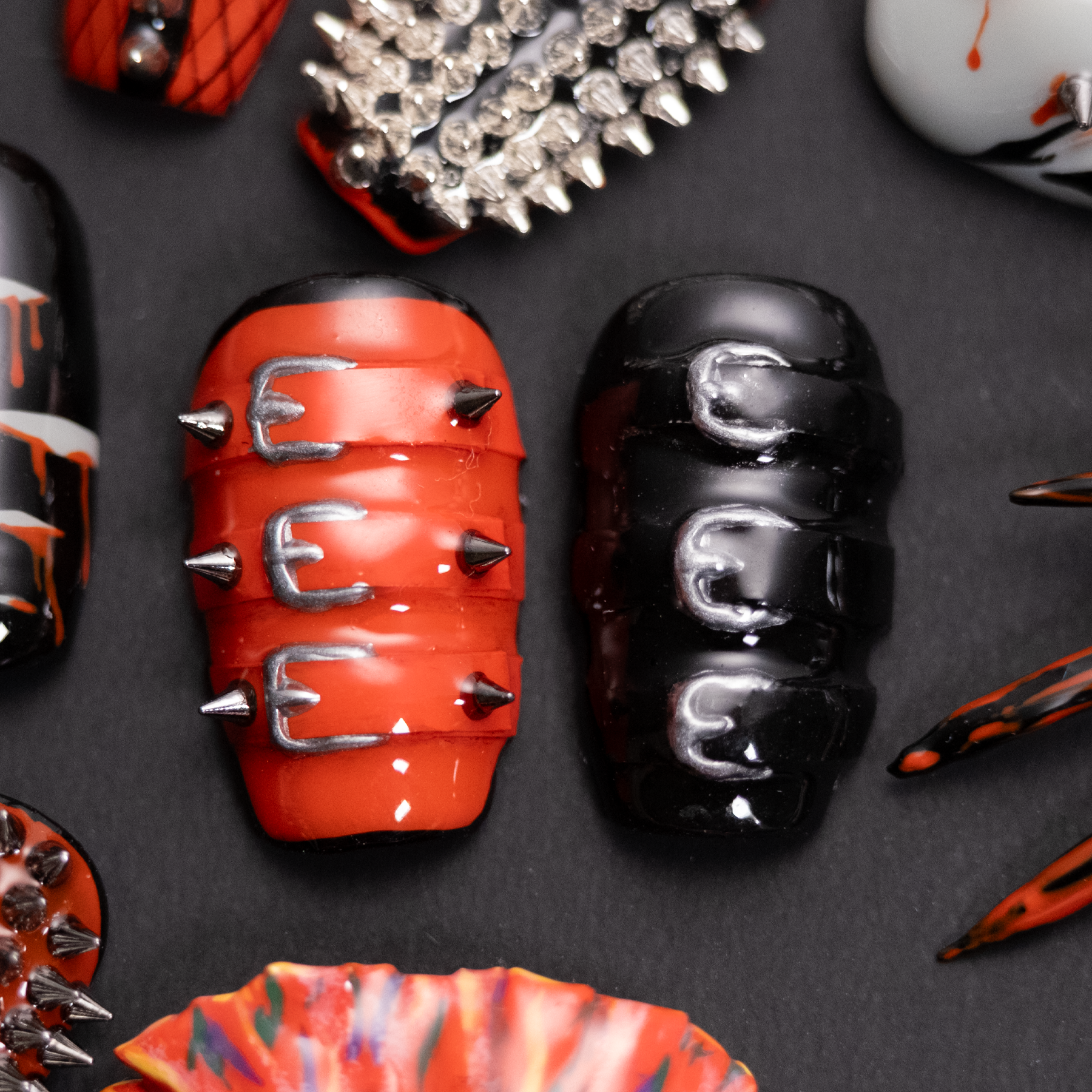 A close-up of two punk-inspired press-on nails, one in red with silver spikes and buckles, the other in black with sleek buckle designs, exuding edgy style.