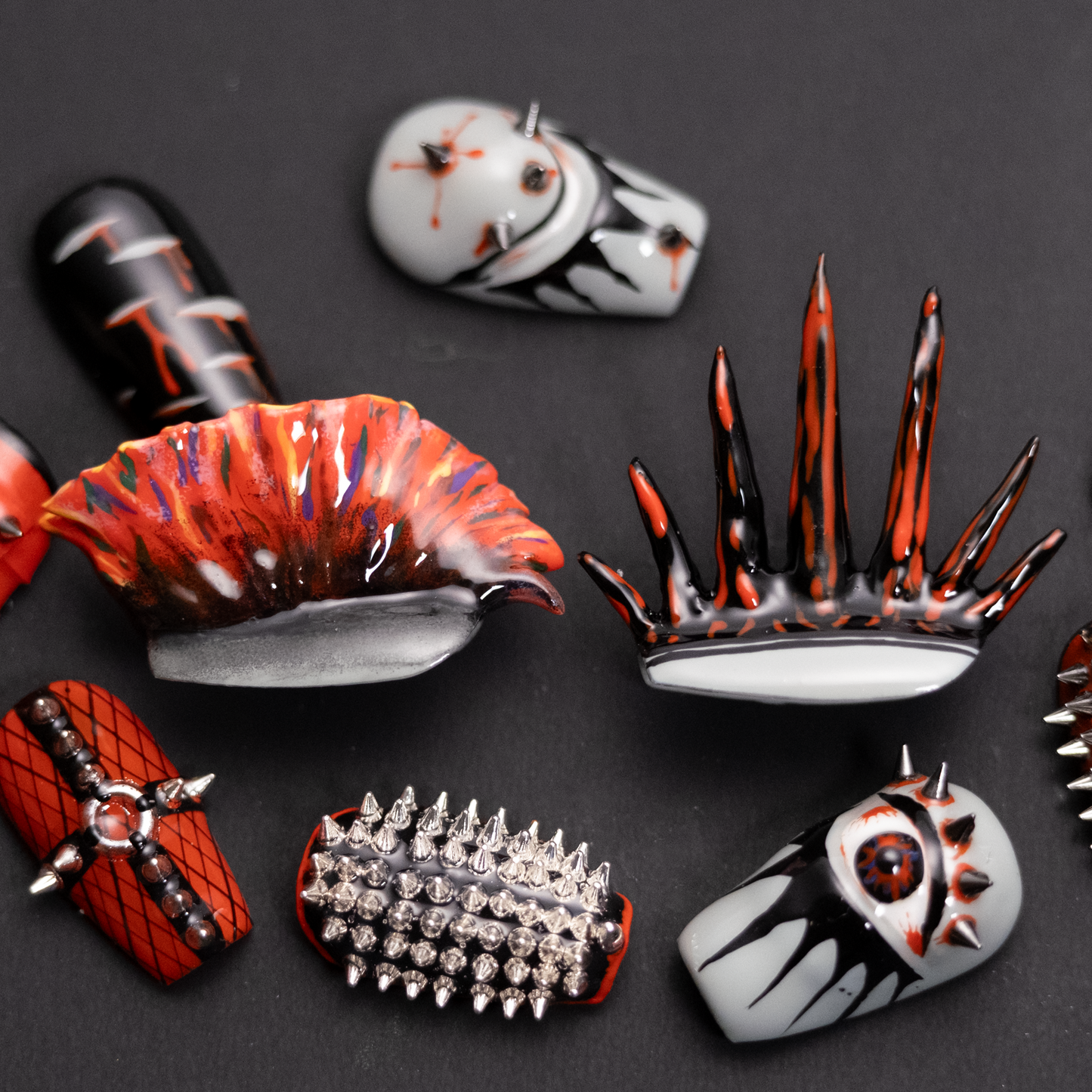 A set of bold, punk-inspired press-on nails featuring spikes, studs, and intense designs in red, black, and silver, with 3D elements.