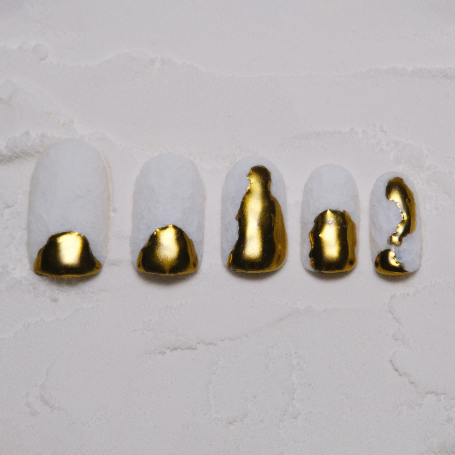 A set of press-on nails with a textured white base and bold gold accents that appear as if the nail tips were dipped in gold, creating a luxurious look.