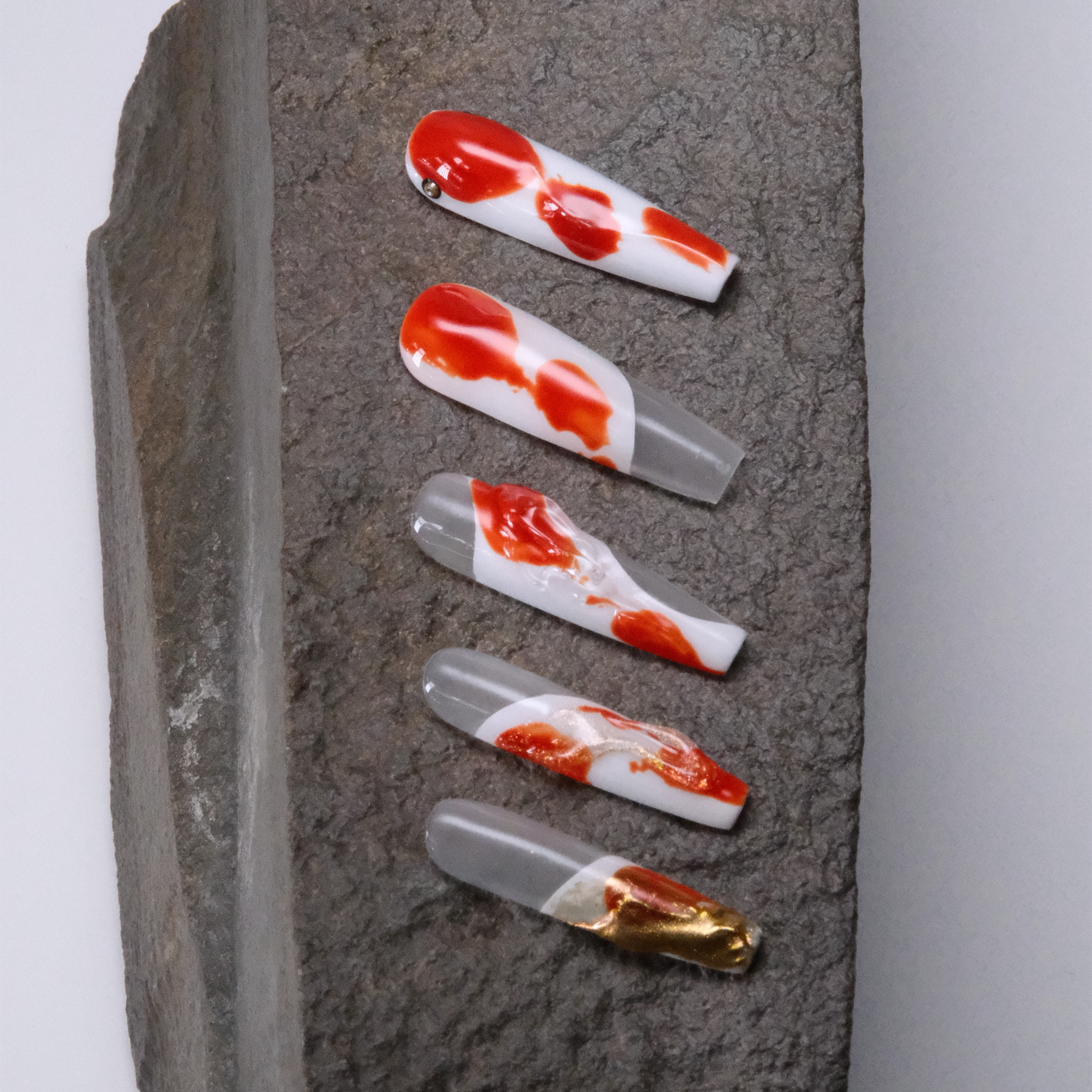 A set of koi-inspired press-on nails with flowing red, white, and gold designs arranged on a stone surface, symbolizing good luck and elegance.