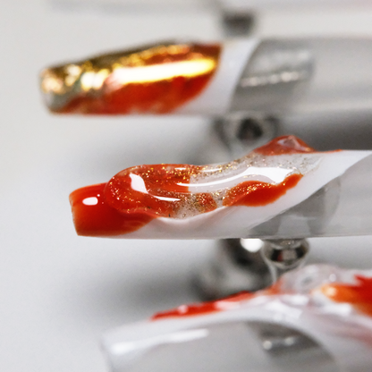 A close-up of koi-inspired press-on nails, symbolizing good luck in oriental culture, with flowing red, white, and gold swirls and a glossy 3D finish.