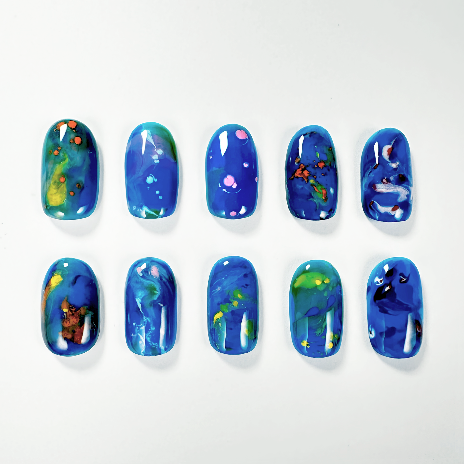 A set of nuance press-on nails featuring vibrant blue backgrounds with abstract designs in green, yellow, and pink, evoking a cosmic or oceanic theme.