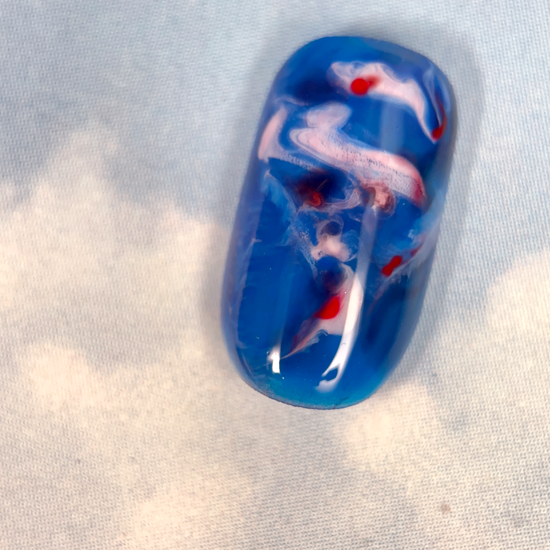 A close-up of a nuanced press-on nail with a deep blue base, featuring swirling white and red tones, creating a dreamy, cloud-like effect.