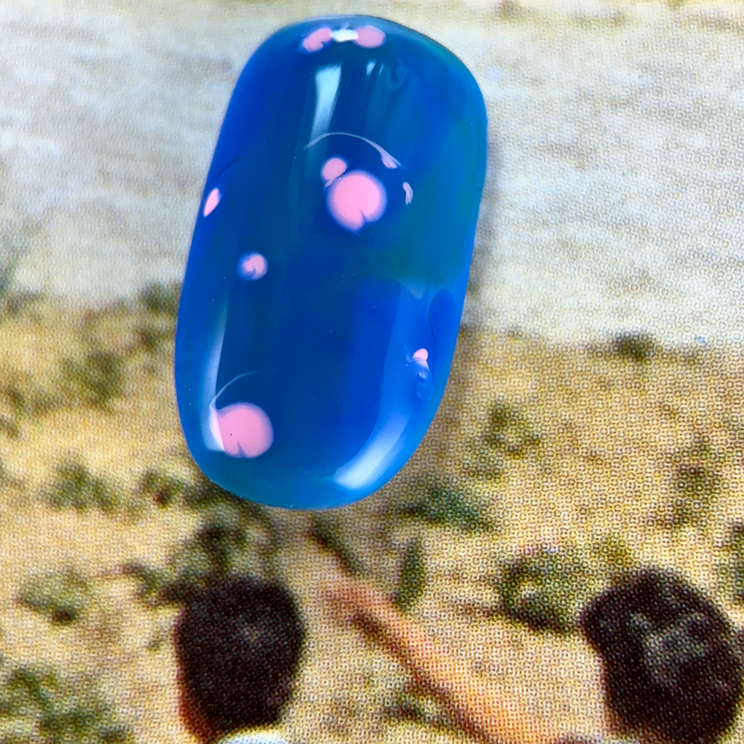 A close-up of a nuanced press-on nail with a vibrant blue base, featuring delicate pink dots, creating a soft and abstract design.