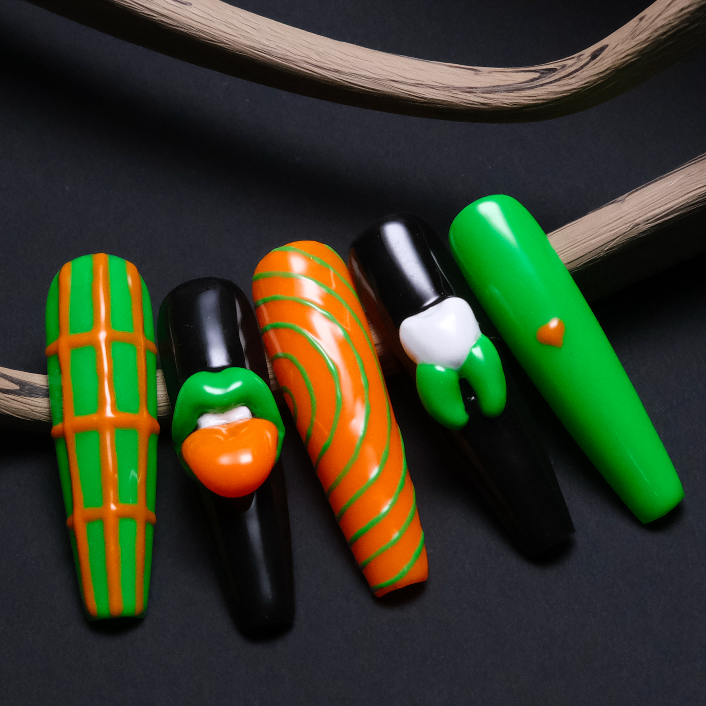 A close-up of five Gothic-inspired press-on nails featuring bold green and orange designs with striking 3D lip and tooth accents, creating an edgy and artistic look.