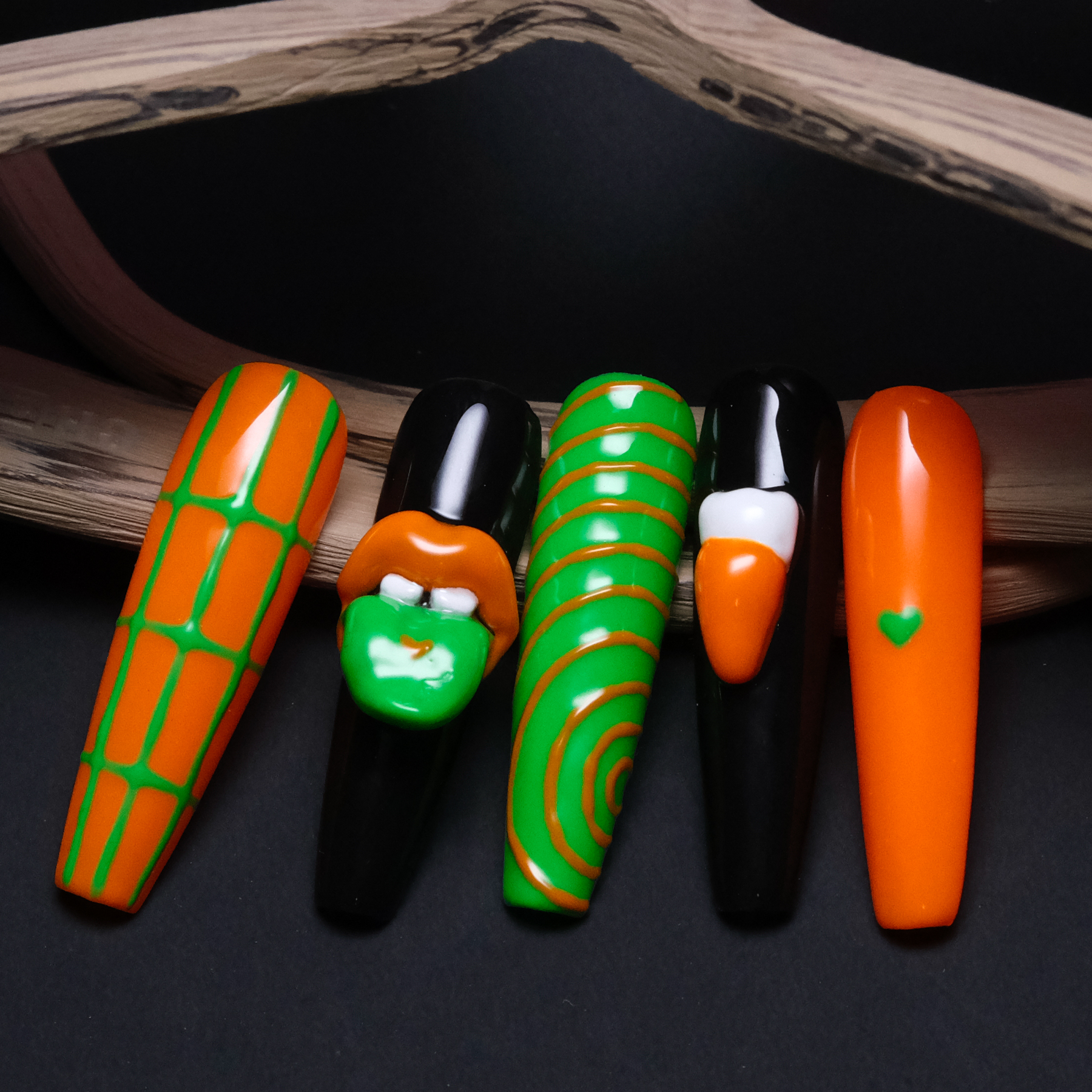 A close-up of five Gothic-inspired press-on nails, featuring bold green and orange designs. The set highlights intricate 3D lip and tooth details for a striking, edgy look.